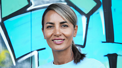 Frau mit blond-braunen Haaren im Sportoutfit vor einer Graffiti-Wand.