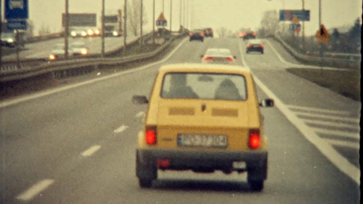 Gelbes Auto fährt auf einer Autobahn. Man sieht es von hinten. Bild sieht etwas altmodisch aus.