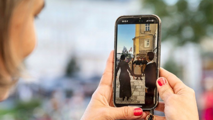 Person hält Smartphone mit Foto von drei Personen vor historischem Gebäude