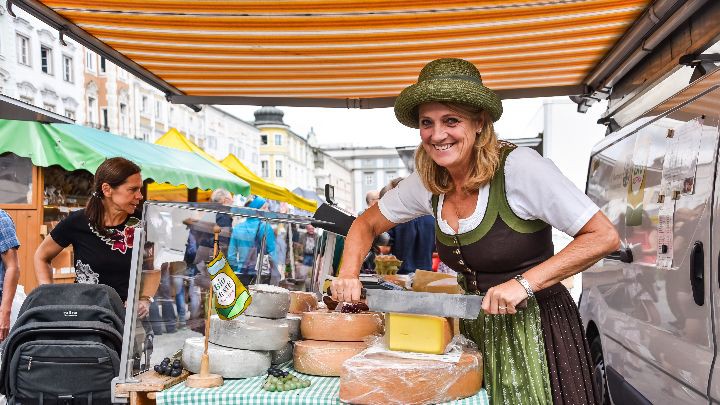 Eine Käseverkäuferin schneidet von einem großen Käselaib ab.