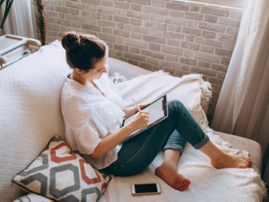 Junge Frau auf einer Couch sitzen mit einem Tablet in der Hand