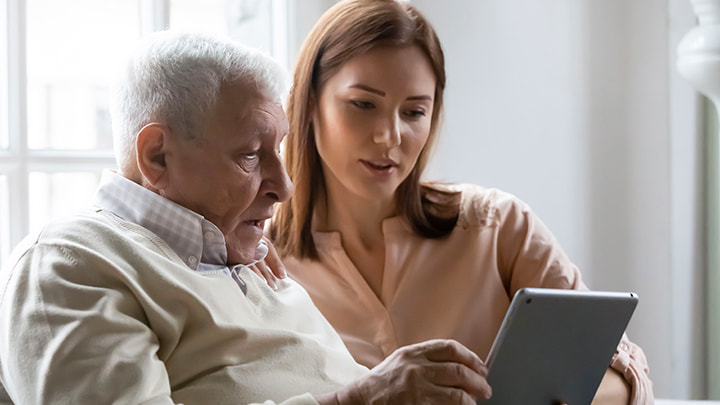 Eine junge Frau und ein älterer Mann schauen auf ein Tablet